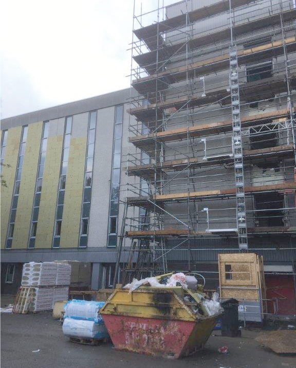Rear building façade nearing completion with insulation and scaffolding.