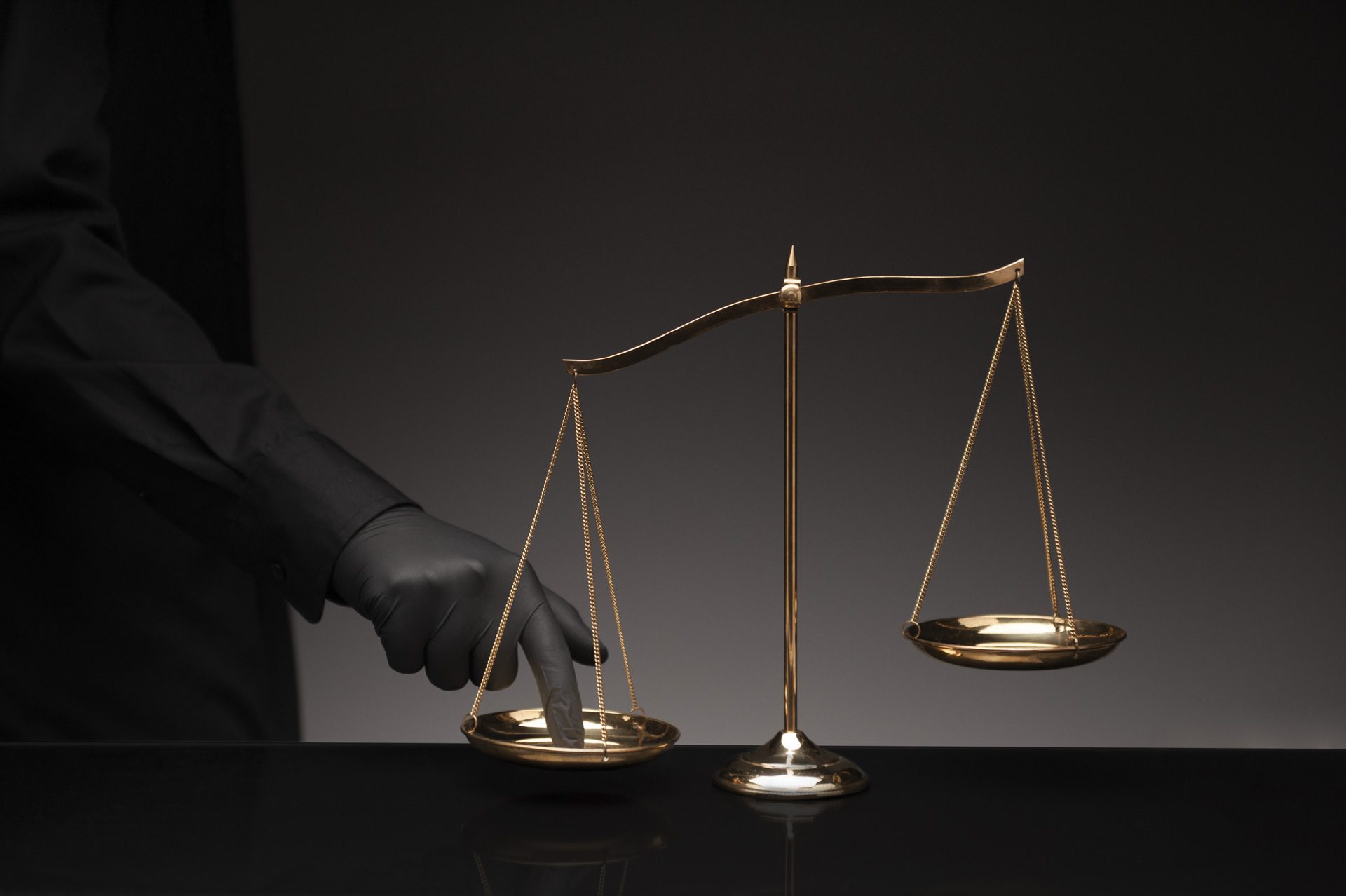 Someone wearing black shirt pressing the imbalance scale on black glass desktop and black background, cheating in a lawyer's office, Concept of injustice, espionage, partiality, law.