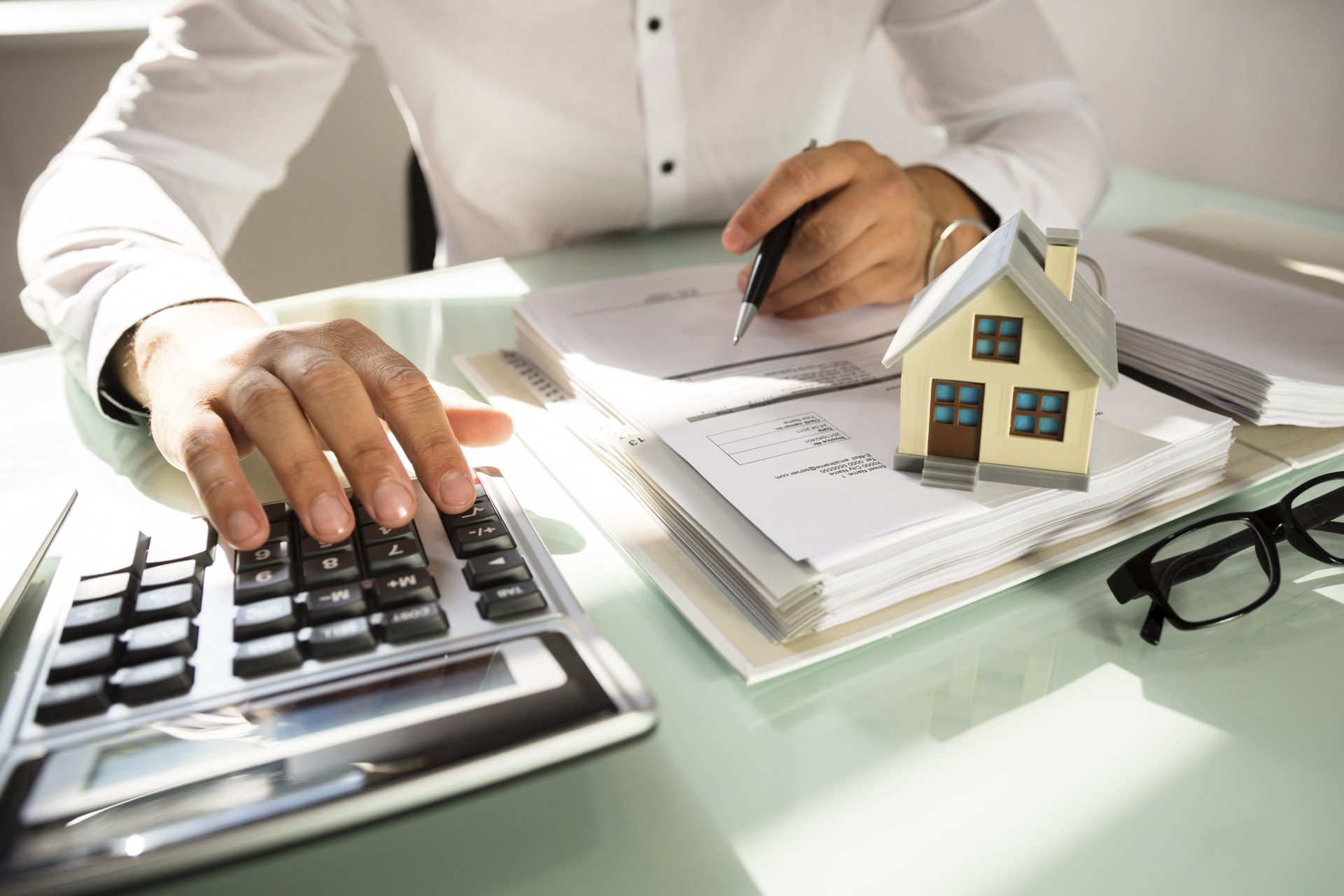 Businessman's hand calculating invoice with house model in office