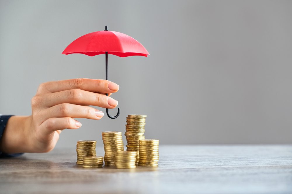 hand holds umbrella above piles of coin