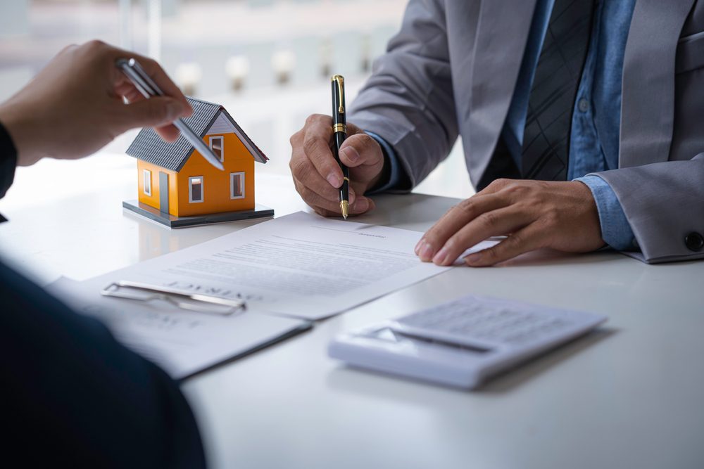 Agent and property investor discussing a real estate opportunity and signing contracts with a model house on the desk
