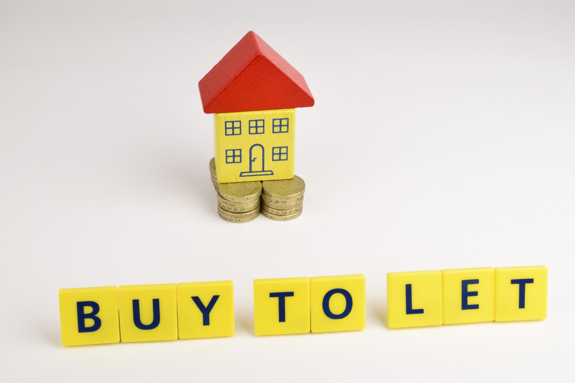 A toy house sitting on a stack of coins with the words, 'Buy To Let' in front of it.
