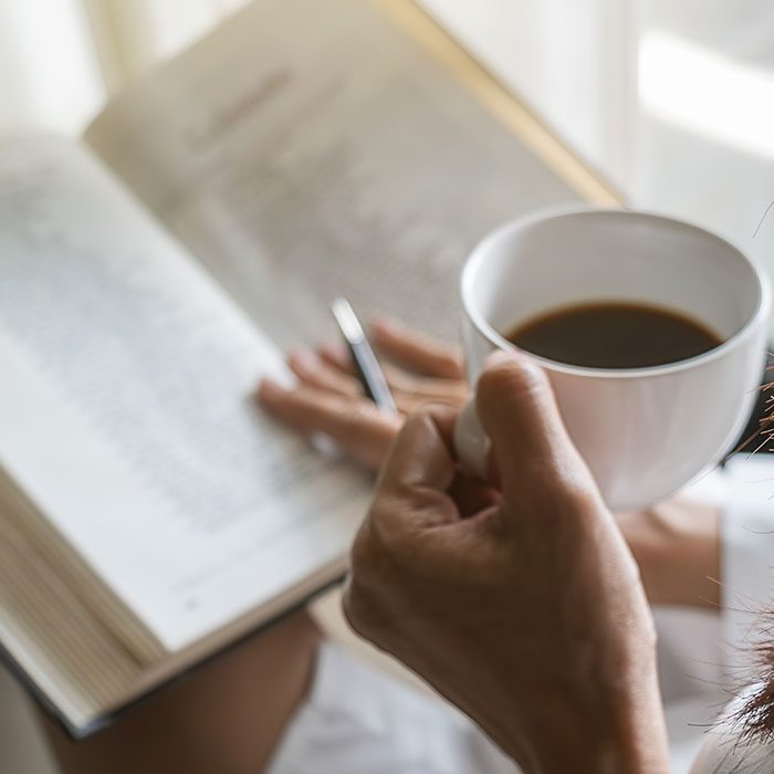 A person reading book with a cup of coffee in her hand