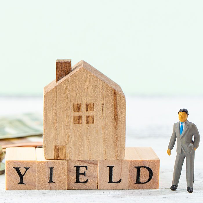 Human figure standing next to a house model and blocks written YIELD.