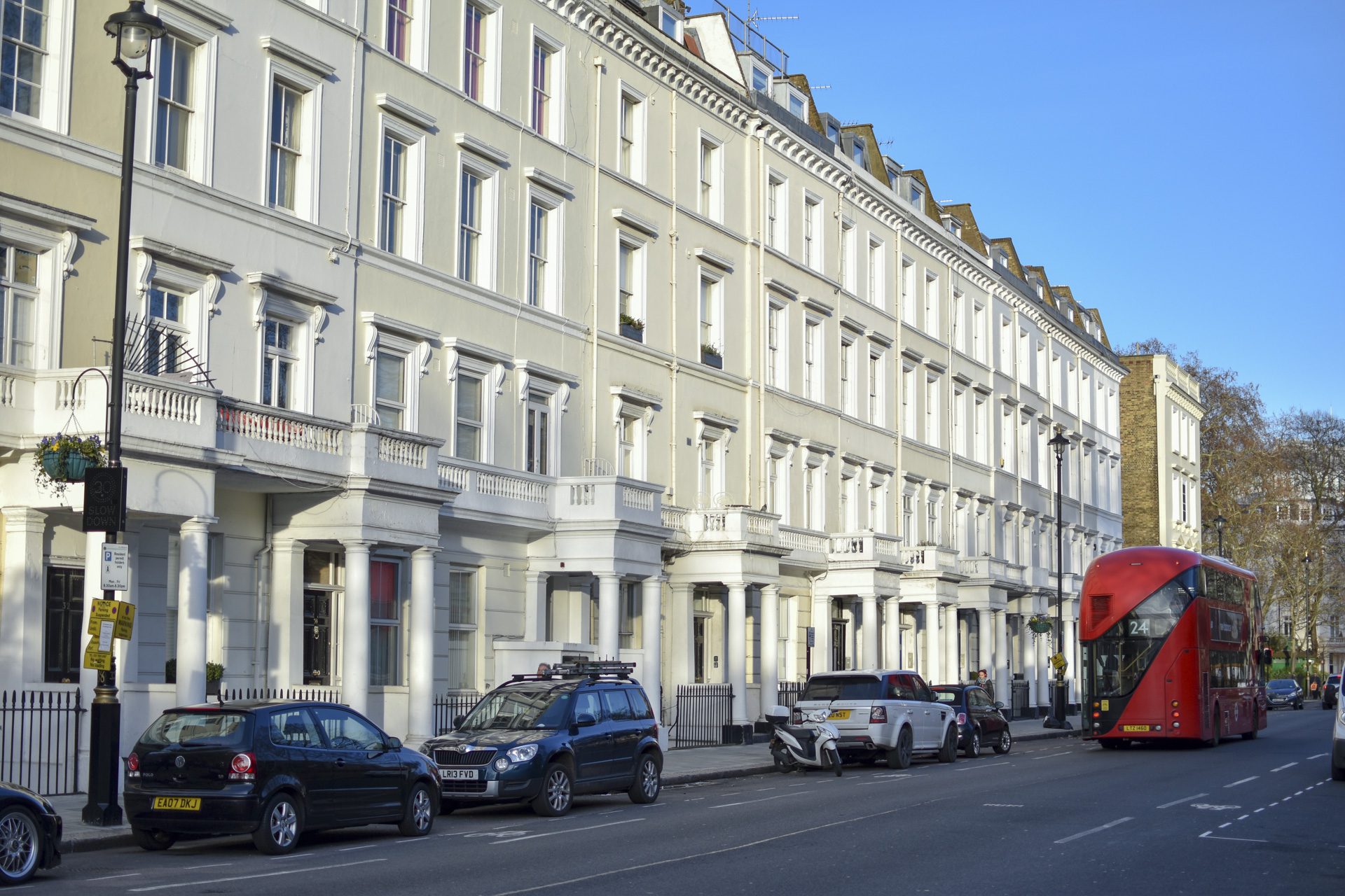 London, UK - February 2 2019: Street view of Lupus street, Pimlico, traditional white townhouses, red London double decker bus driving by, early evening sun -Image