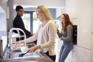Students inside UK HMO rental property kitchen, washing dishes and talking