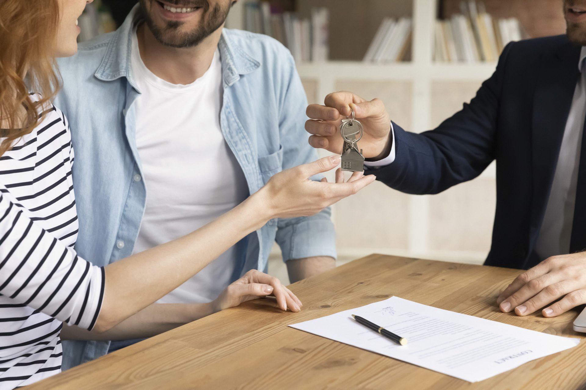 Cropped close up view happy couple receiving keys from new own property, finish meeting in real estate agency lead by realtor in formal suit. Bank mortgage for young family, selling, renting concept