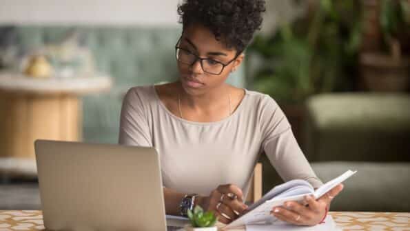 Lady flips book and looking at her laptop