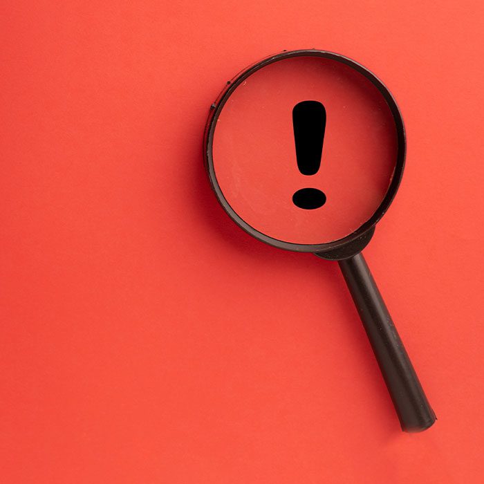 An exclamation mark inside a magnifier with red background