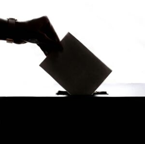 hand putting a voting slip into a ballot box