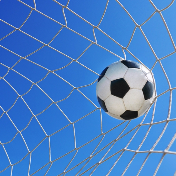 Football in goal net in a big stadium isolated on blue sky.