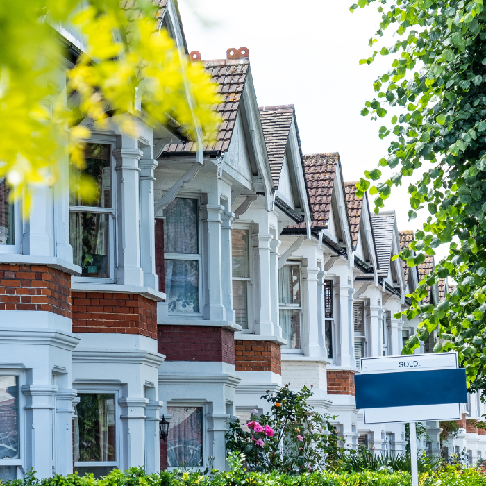 Row of terraced houses with 'sold' sign on a street with trees