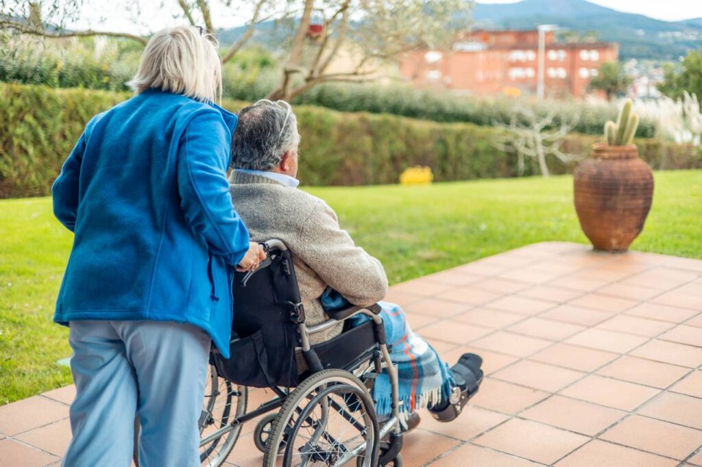 Nurse pushing elderly patient in wheelchair in garden of retirement home