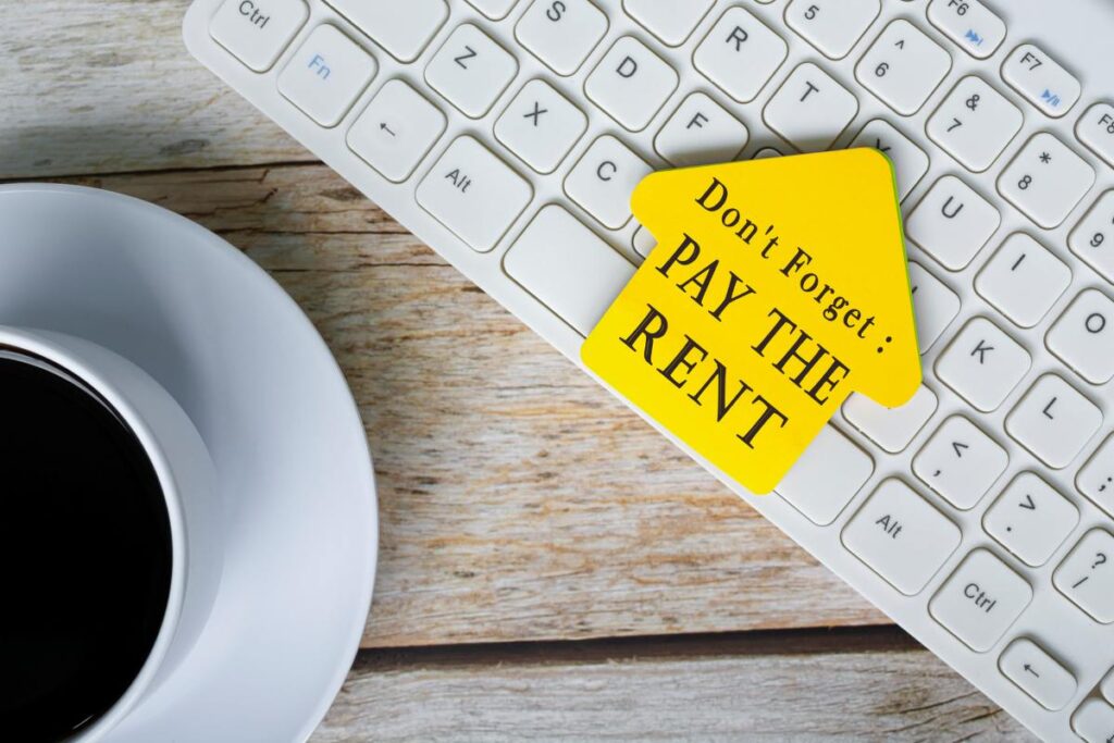 Don't forget, pay the rent text on yellow stick house shape on white keyboard