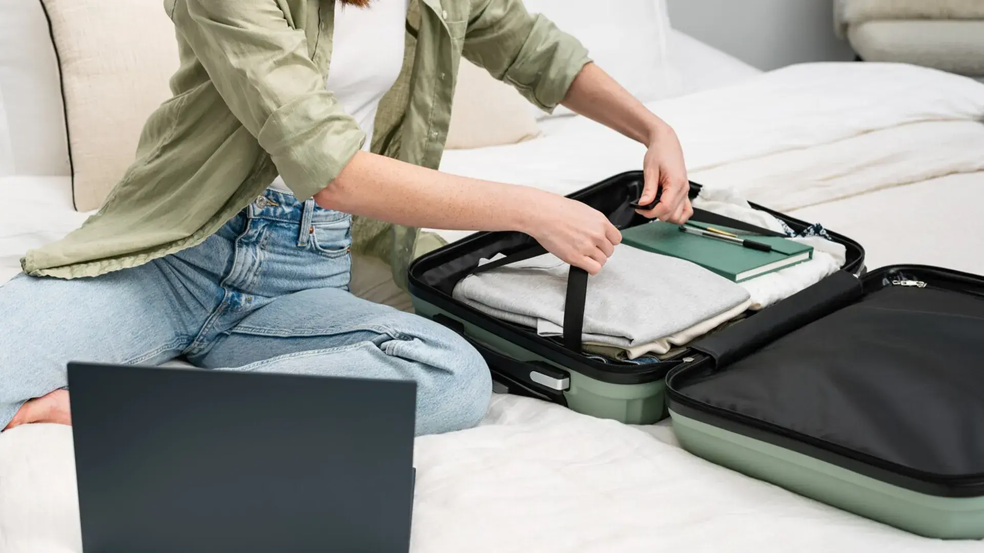 Person sitting on a bed unpacking a suitcase