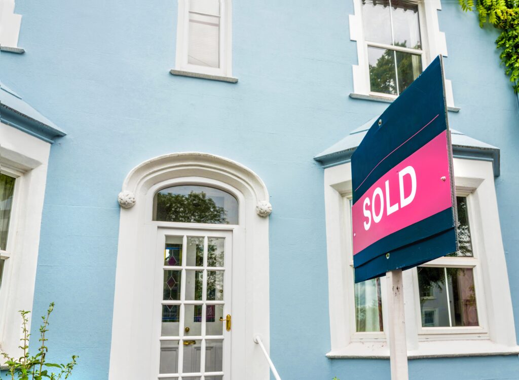 Estate agent sold sign in front of a blue house