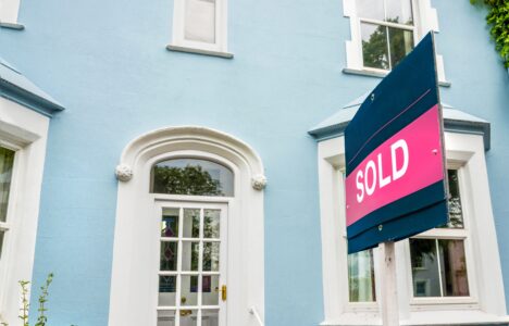 Estate agent sold sign in front of a blue house
